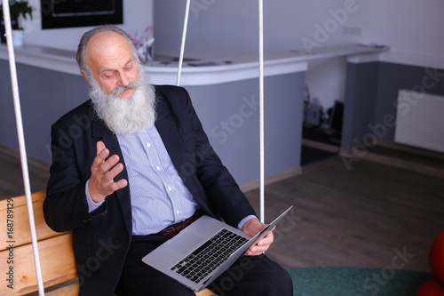 Old retired man prints on laptop and talks with colleagues behin photo