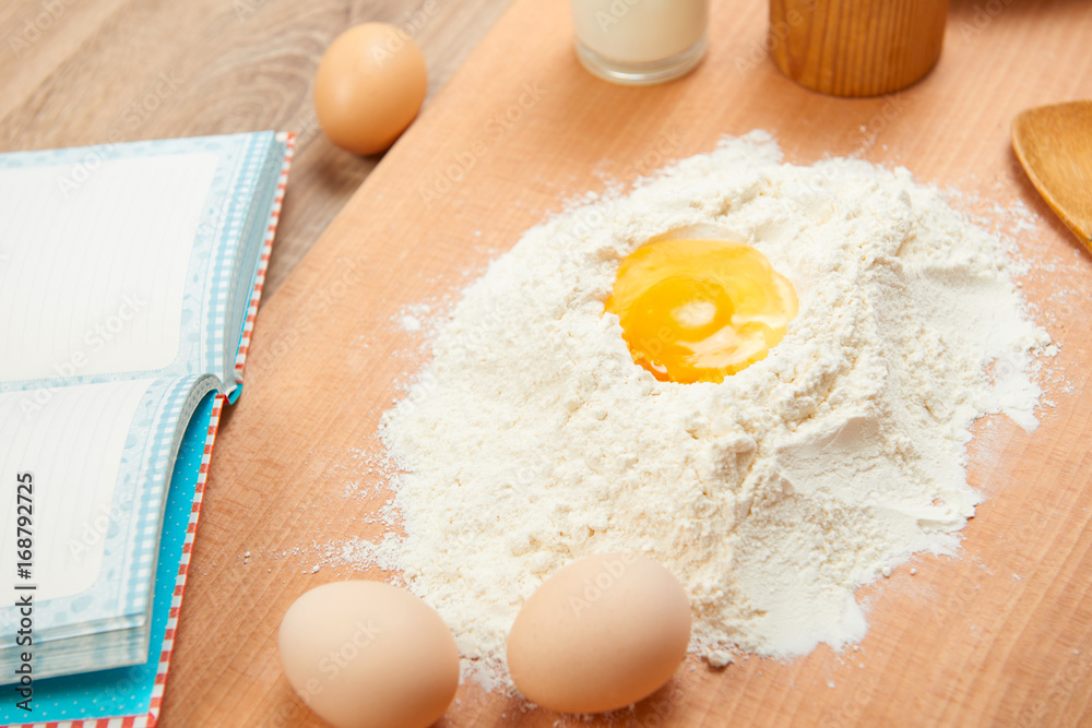 Flour heap and broken egg closeup for baking on a wooden background. Raw food and kitchen utensils. Flour heap and broken egg closeup for baking on a wooden background. Raw food and kitchen utensils.