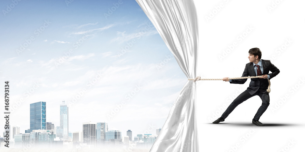 Obraz premium Young man opening white curtain and presenting modern city landscape