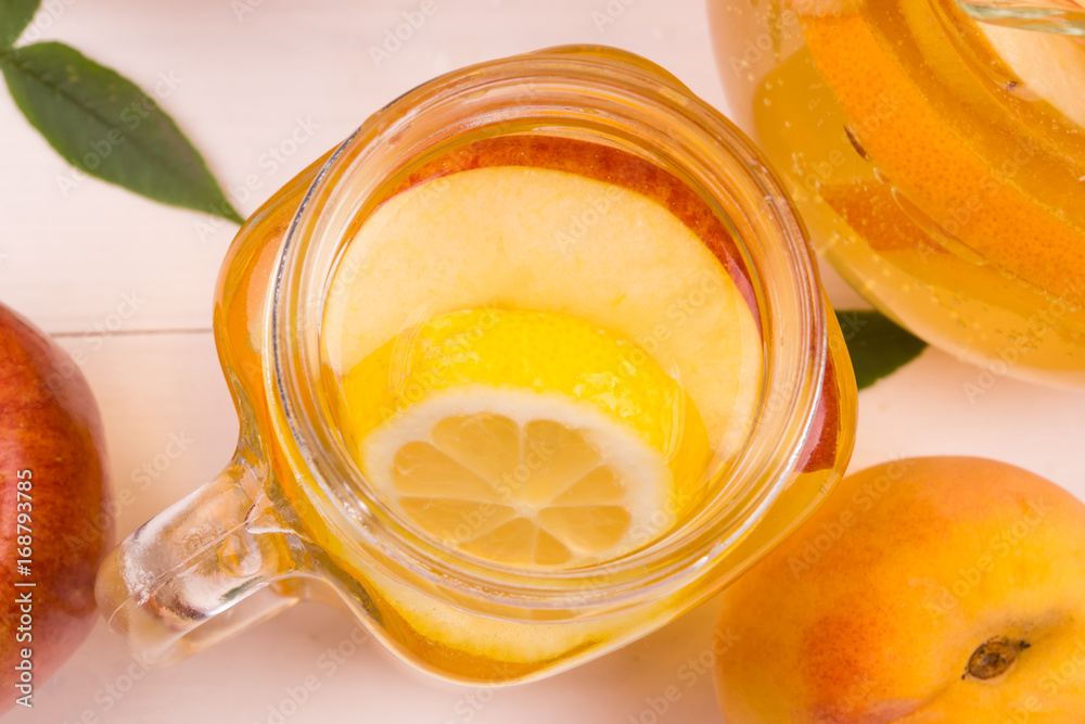 Sparkling White Peach Sangria apples, oranges and lemons on a white rustic wooden background. Jug with a cool fruit drink. Top view