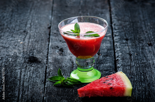 Water melon cocktail with slices of fresh melon on a wooden burnt table with ice cubes. Black natural background. Healthy drink. Summer cocktail