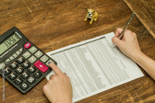 Mão de mulher analisando planilha de custos, utilizando calculadora, trabalhando, visto de cima  photo