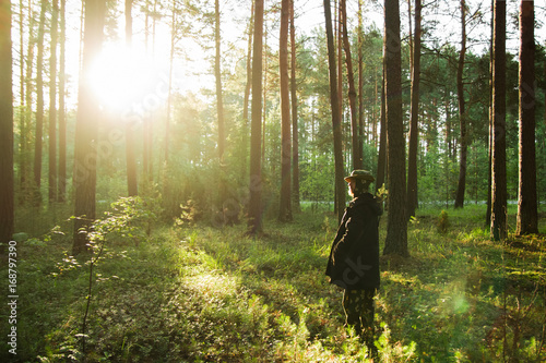 Φωτογραφία Young man in a black jacket is walking in a pine forest on sunrise