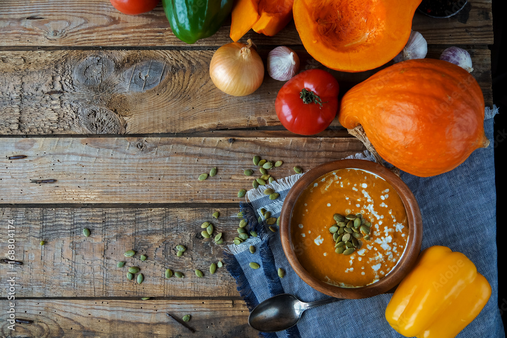 Traditional homemade pumpkin soup with seads, cream and vegetables on rustic wooden table Traditional homemade pumpkin soup with seads, cream and vegetables on rustic wooden table