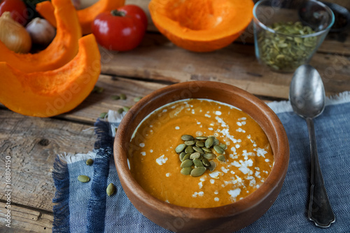 Traditional homemade pumpkin soup with seads, cream and vegetables on rustic wooden table