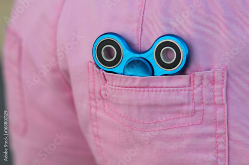 Blue metal popular fidget spinner in the back pocket of pink jeans, anxiety relief toy, anti stress and relaxation fidgets photo