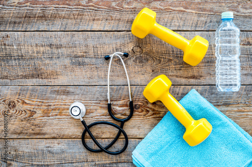 Sport and health. Fitness. Dumbbells and stethoscope on wooden background top view copyspace