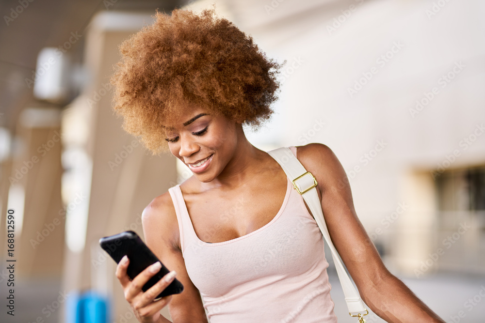 african american woman checking flight on smartphone at airport with luggage african american woman checking flight on smartphone at airport with luggage