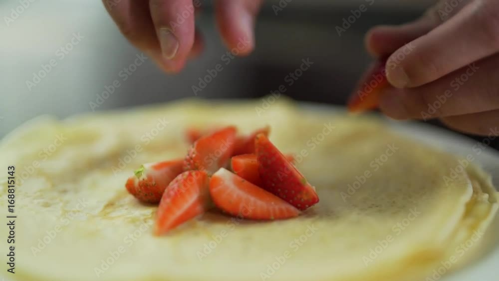 Man lays strawberries on pancakes.
