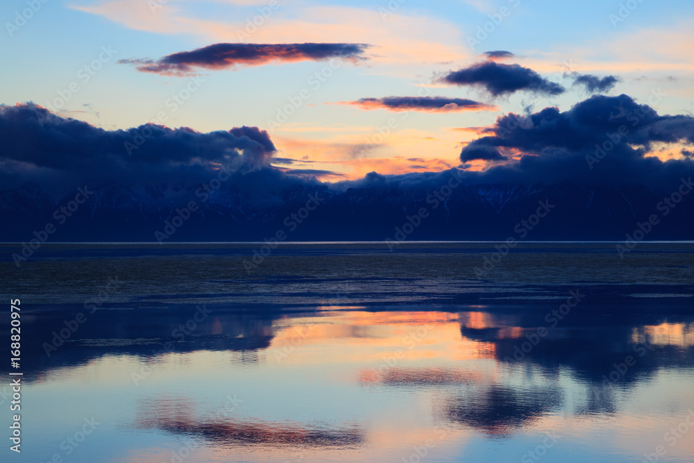 Dramatic sunset over water surface of mountain lake with clouds reflection, colorful landscape