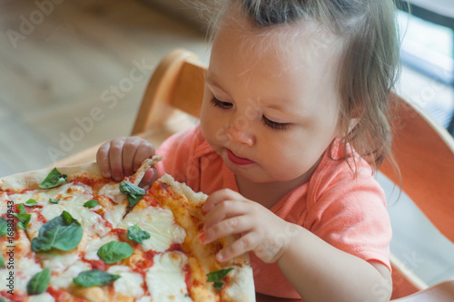 One Year boy sits in director chair in a public cafe indoor and eating italian pizza  children s fast food