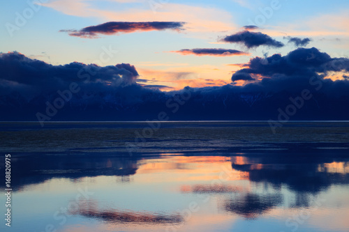Dramatic sunset over water surface of mountain lake with clouds reflection, colorful landscape