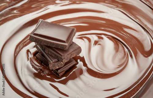 Melted pieces of chocolate bar in glossy chocolate splash background.