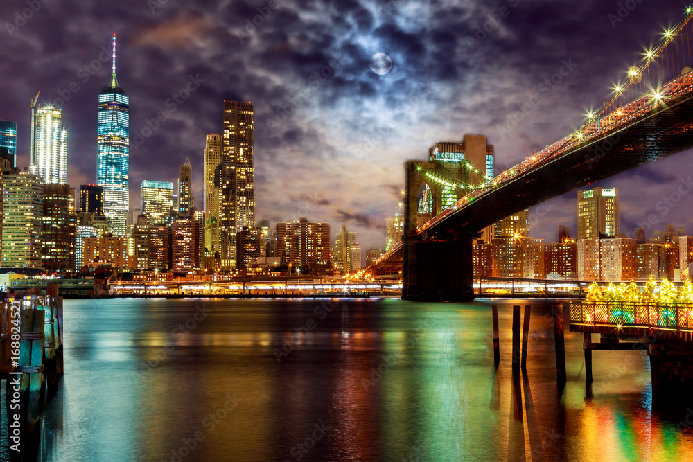 New York City's Brooklyn Bridge and Manhattan skyline illuminated full moon overhead.