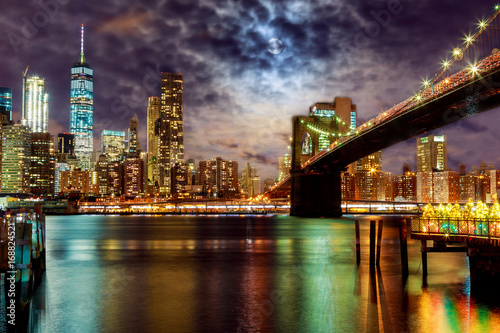 New York City's Brooklyn Bridge and Manhattan skyline illuminated full moon overhead. © ungvar