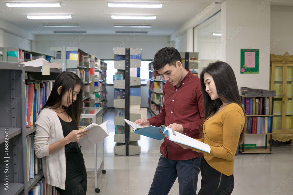 Group of happy students with books talking and preparing to exam in library. Education concept.