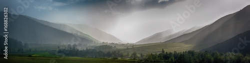 fluffy rainy clouds over green hills at foggy sunrise
