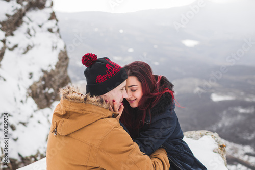 Couple sitting on edge of cliff in mountains with beautiful view. Winter and snow