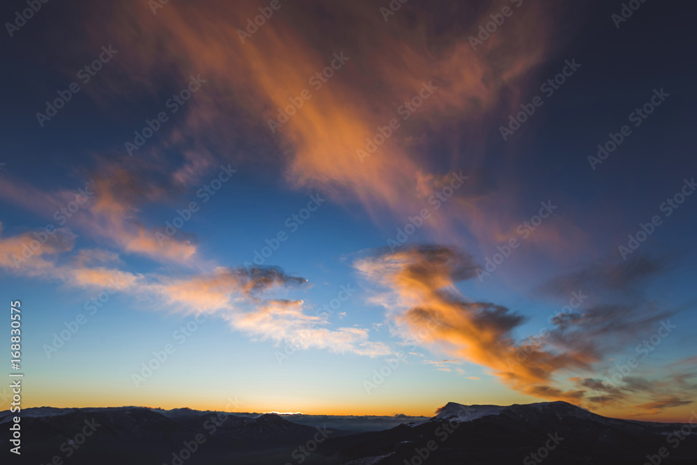 Amazing colorful sunset high in mountains. Orange clouds and blue sky