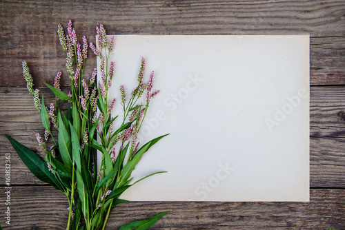 Sheet of paper and the little pink flowers on wooden background