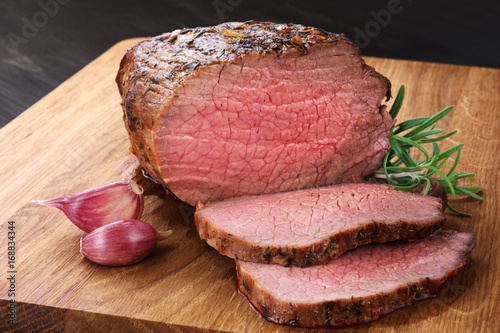 Baked meat, garlic and rosemary on a wooden background. Roast beef.