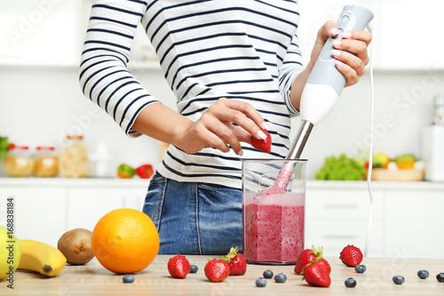 Young woman cooking smoothie in blender