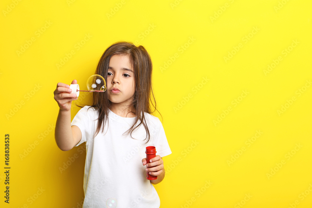 Beautiful little girl blowing soap bubbles on yellow background Beautiful little girl blowing soap bubbles on yellow background