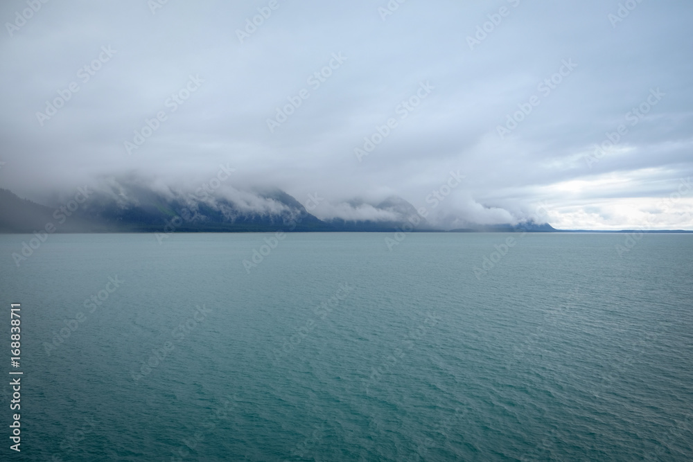Fototapeta premium Sun breaking through cloud covered mountains overlooking a green ocean