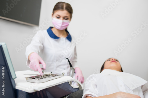 Beautiful woman dentist doing first check-up for female patient at the dental office. Doctor taking dental tools wearing mask and gloves. Medical equipment. Stomatology