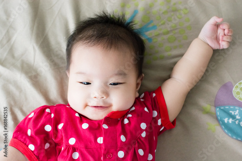 Portrait of adorable baby girl lying on back on the bed and looking in camera indoors