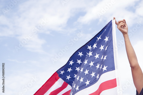 Man hand holding American flag with blue sky.