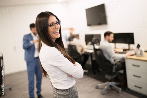 Businesswoman posing while other businesspeople talking in background photo