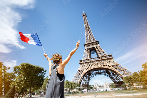 Young woman tourist standing back with french flag enjoying view on the Eiffel tower in Paris