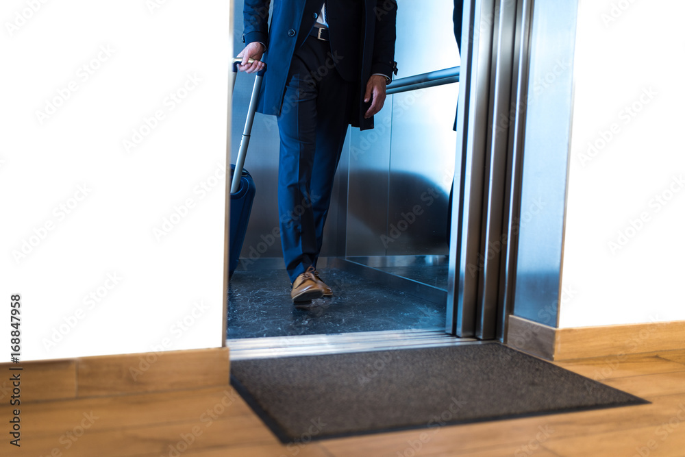 Businessman in suit comes out from elevator with a baggage  