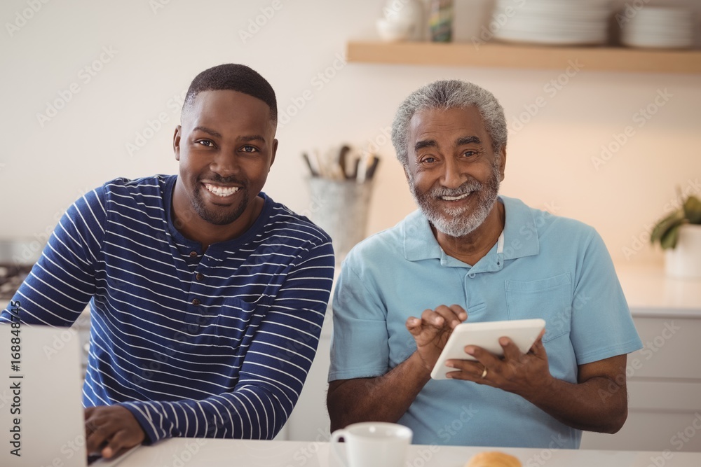 Smiling father and son using laptop and digital tablet in kitchen Smiling father and son using laptop and digital tablet in kitchen