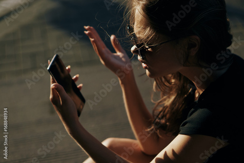 Beautiful woman holding a phone on the street at sunset in the sun