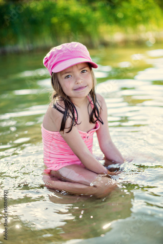 Fototapeta Naklejka Na Ścianę i Meble -  Portrait kid girl in pink cap swimming in lake water
