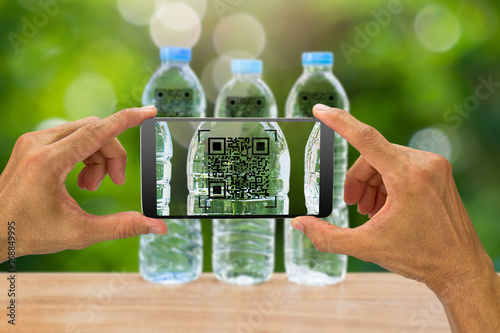 Man's hands holding smartphone scanning QR code on drinking water bottle in the garden, business concept