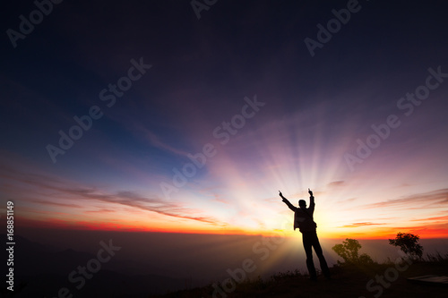 Silhouette of a man standing on the cliff looking at sunrise background, hope and following a dream concept