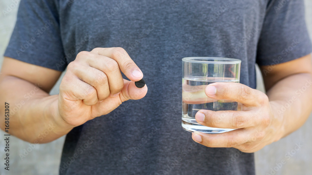 Man holding an activated charcoal pills and a glass of water. Man holding an activated charcoal pills and a glass of water.
