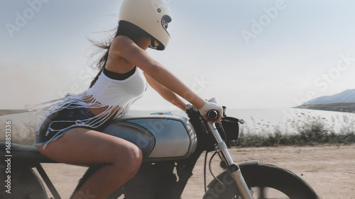 Sexy female in protective helmet riding fast on her custom built cafe racer motorcycle in the desert photo