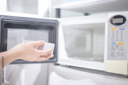 woman hand using are bringing food into the microwave oven at home. To reheat frozen food for their . Cooking made easy concept .