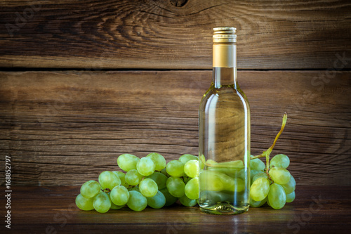 A bottle of white wine with grapes on a wooden background
