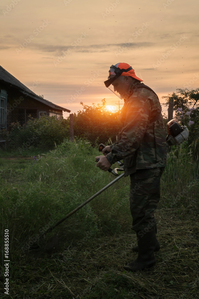 A man mows the grass in the garden with a trimmer at dawn A man mows the grass in the garden with a trimmer at dawn