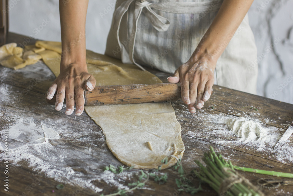 The young woman rolls out the dough with a rolling pin on an old wooden table The young woman rolls out the dough with a rolling pin on an old wooden table