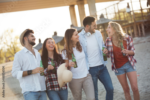 Group of young cheerful friends walking and drinking beer