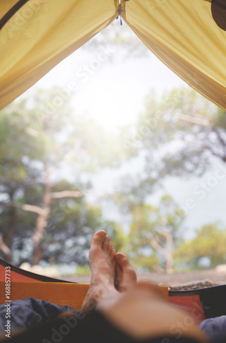 view from inside a tent at the forest and male legs emerge from tent. travel and hiking concept. Tourist tent inside with men's feet. © vitaliymateha