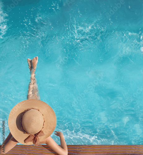 Back view of woman in straw hat relaxing in turquoise water swimming pool at luxury villa resort. Summer holiday idyllic background. Vacations Concept. Exotic Paradise.