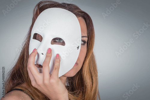 Young emotional woman holding mask in a hands pose in studio on gray background