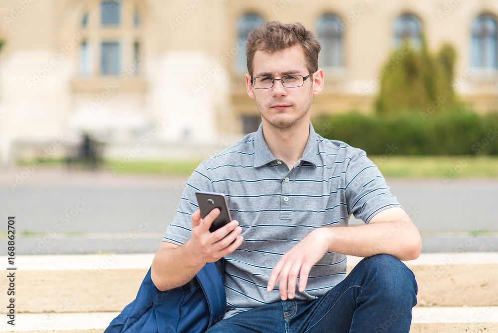 Obraz premium Young man sitting on the stairs with his phone